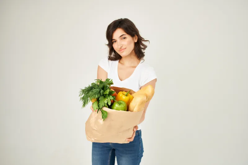 Женщина с пакетом полезных продуктов, доставка из супермаркетов, светлый фон