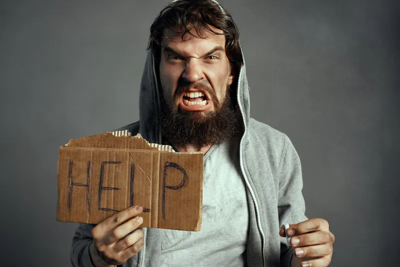 Бездомный бородатый мужчина, бродяга с сигаретой и табличкой «Help»