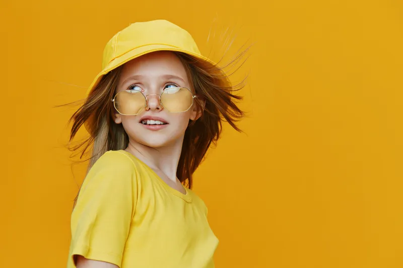 Young girl in yellow outfit and sunglasses on a vibrant yellow background, showcasing a playful and carefree summer mood, perfect for seasonal themes and fashion