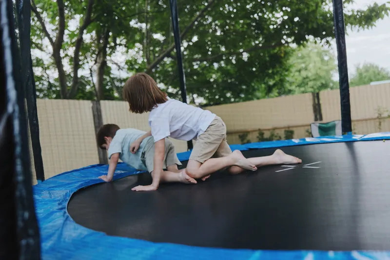 Two children playing joyfully on a trampoline, showcasing energy and excitement in a vibrant backyard setting filled with green trees.