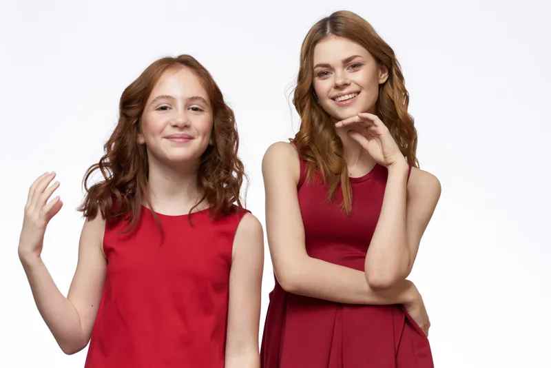 На светлом фоне счастливая мама и дочка обнимаются рядом с красными платьями, улыбаясь