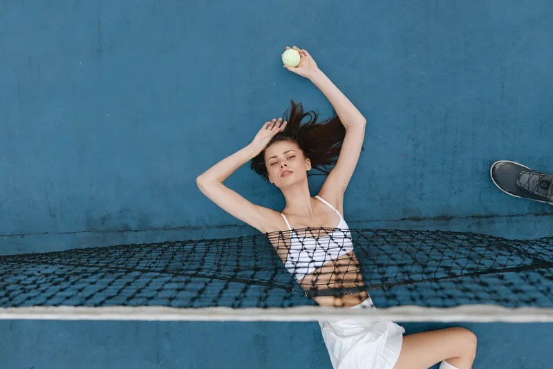 Young female athlete relaxing with a tennis ball on a tennis court, showcasing determination and sports spirit in a bright and cheerful setting