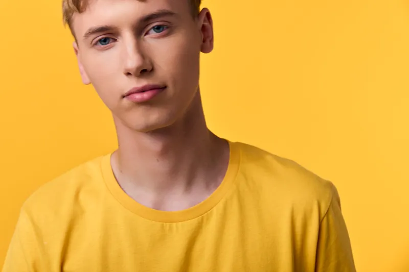 Young man wearing a yellow shirt against a bright yellow background, closeup, studio lighting and clean look ideal for fashion, lifestyle and advertising stock, conveying calm, modernity and