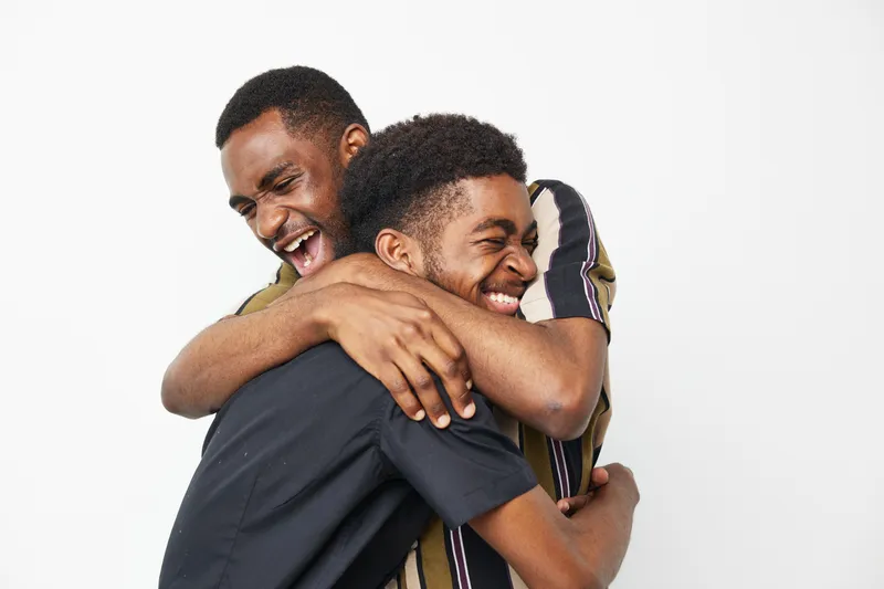 Two joyful African American men share a warm embrace, showcasing friendship and happiness against a simple white background, radiating positivity and connection.