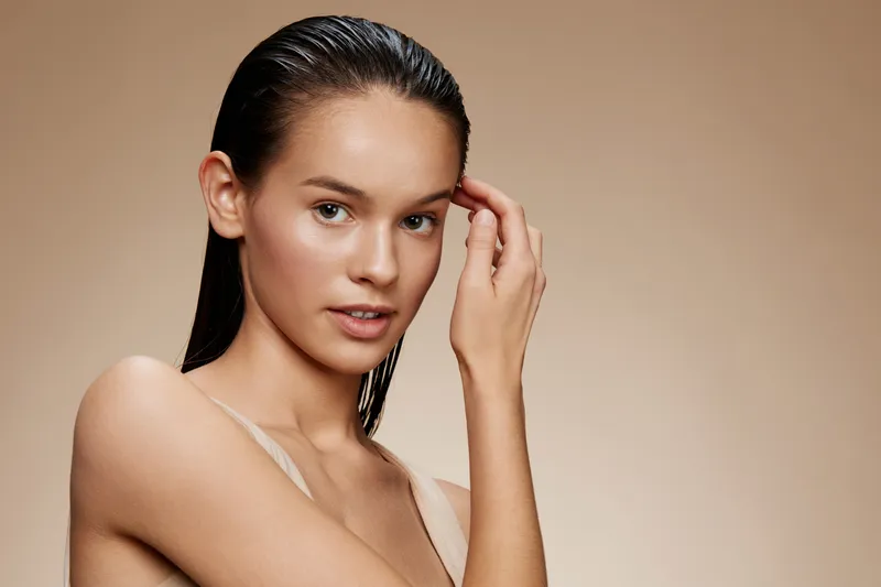 Young model with wet hair and natural makeup, showcasing healthy skin and a subtle smile against a neutral background Perfect for beauty and skincare concepts