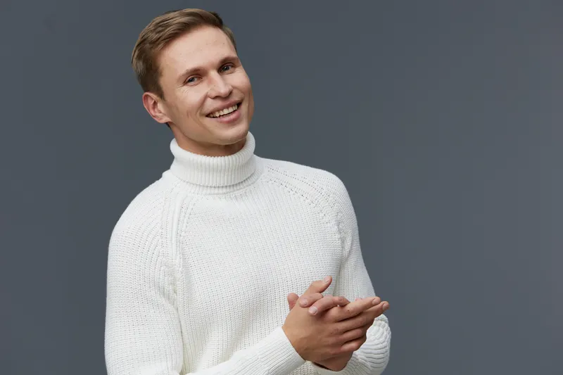 smiling man in white turtleneck sweater posing against grey background digital nomad remote work freelance concept