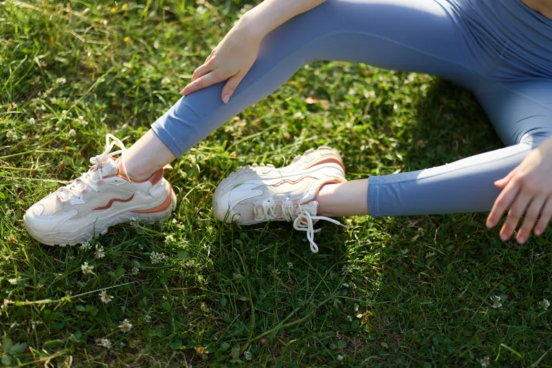 Young woman in activewear stretching on grass, showcasing athletic shoes and a serene outdoor atmosphere with a focus on fitness and well being