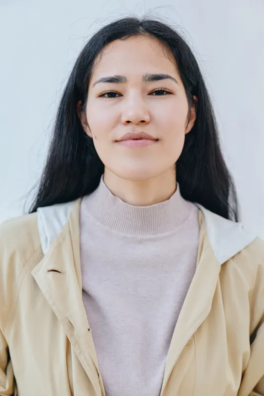 Woman in a beige jacket and soft sweater stands outdoors with a calm, thoughtful expression, showcasing casual fashion and serene mood in natural light for lifestyle and street style photography