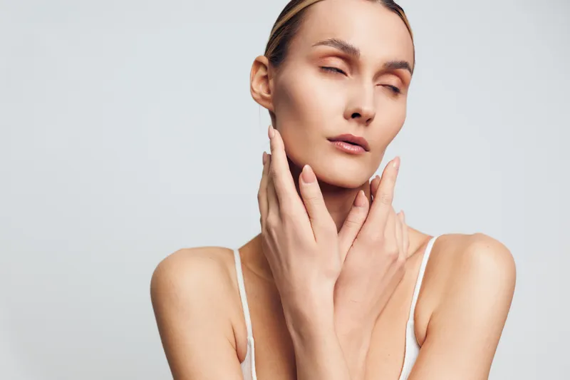 Woman in skincare routine, hands on cheeks, gentle face massage, calm expression, soft studio lighting, close up portrait on neutral background, natural skin texture, beauty care, fresh look