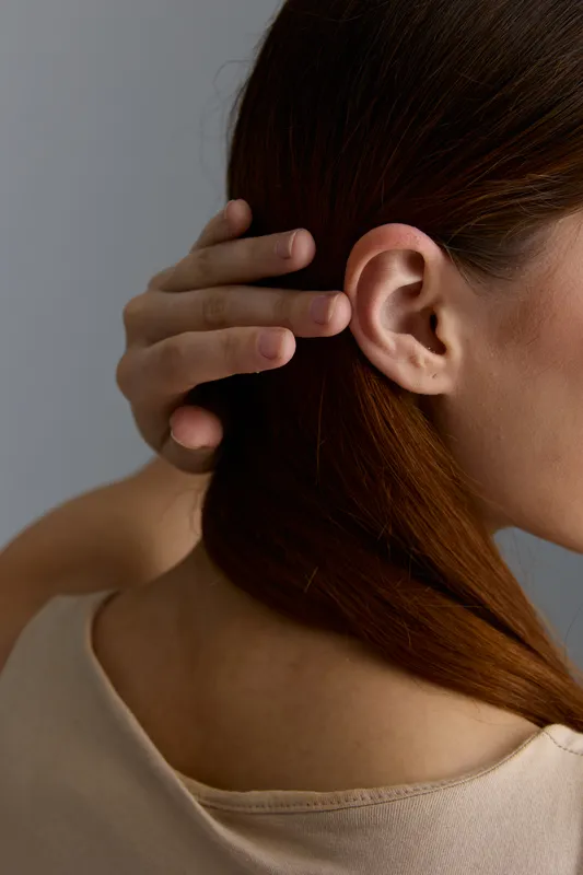Close-up of a beauty woman with red hair gently holding her head, showcasing natural skin and delicate features in soft lighting and neutral background.