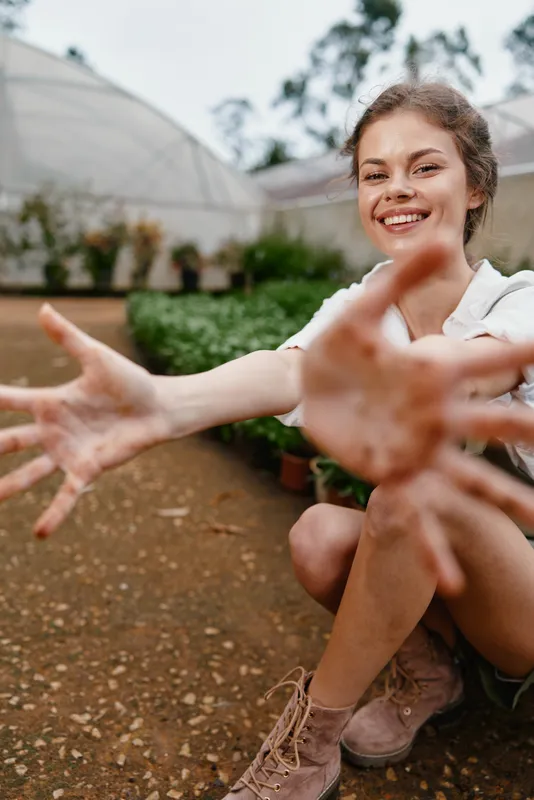 Joyful young woman with dirty hands showing excitement in a greenhouse, representing gardening, nature, and sustainable living through her bright smile and rustic attire
