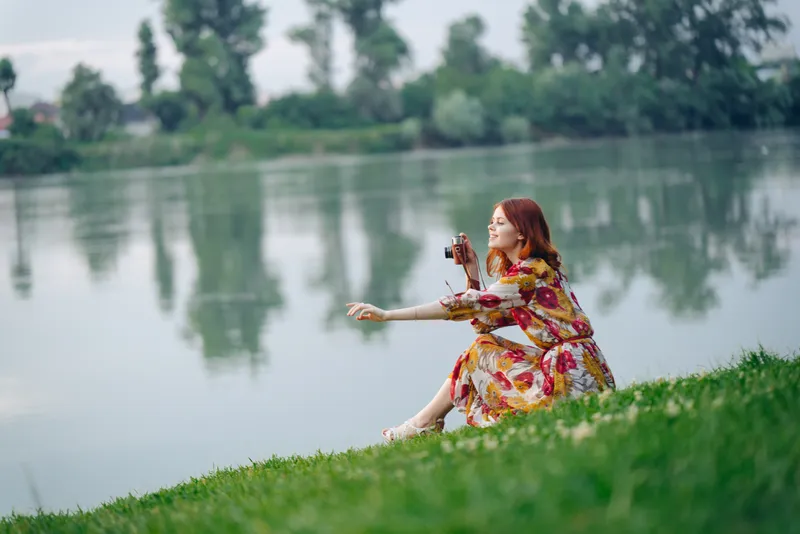 Симпатичная женщина в платье на природе, с фотоаппаратом в руках