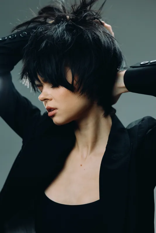 Stylish woman with short black hair posing with closed eyes and thoughtful expression wearing dark jacket
