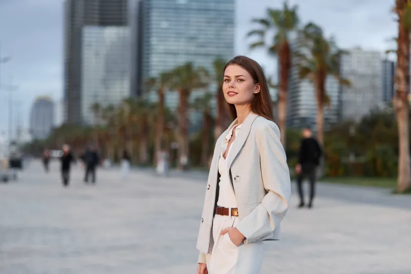 Confident businesswoman in an urban setting, exuding professionalism in stylish attire, surrounded by palm trees and modern architecture.
