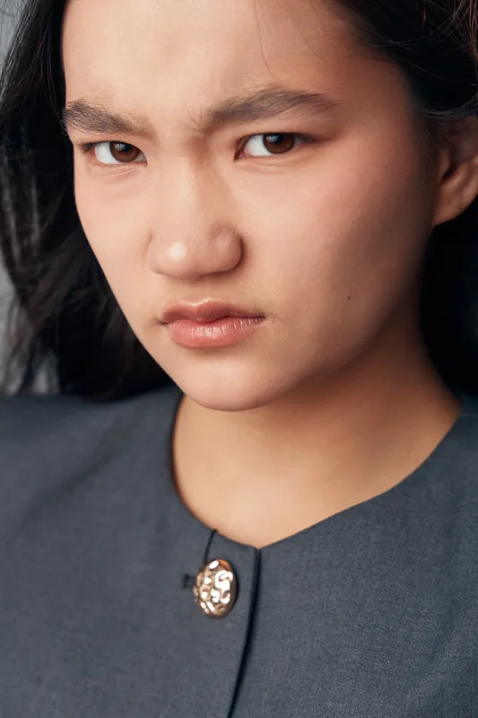 Woman with frown and serious face closeup portrait showing negative emotion, displeasure or anger. Female person with natural makeup and dark hair in casual outfit looking at camera.