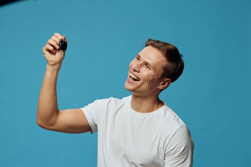 Happy young caucasian man smiling white t-shirt hold car keys isolated blue background digital nomad lifestyle concept