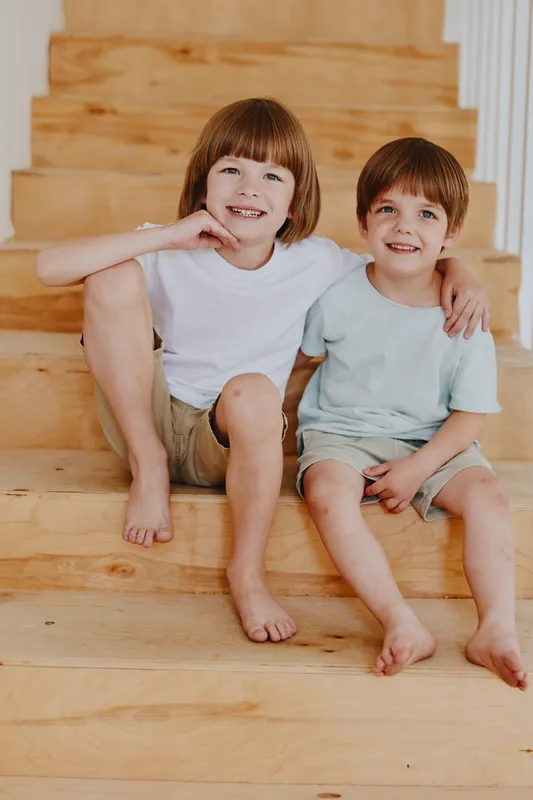 Two happy children, one smiling boy and girl, playfully sitting on wooden stairs in a cozy home setting, capturing the essence of childhood joy.