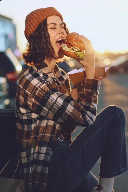 Woman burger eating outdoor candid lifestyle golden authenticity captured at sunset with golden hour glow, mindful living and emotional storytelling in a cozy urban street food moment.
