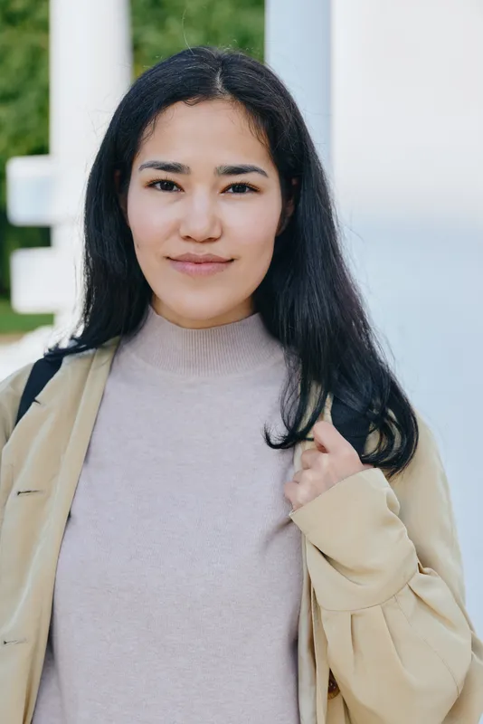 Casual street style, a smiling woman wearing a light sweater and beige coat outdoors, natural light, urban setting, everyday fashion vibe for lifestyle and style photography
