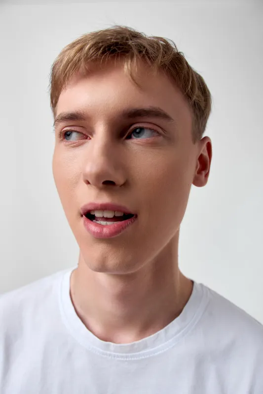 Closeup of a young man wearing a white tshirt, looking to the side with a thoughtful expression, studio lighting, casual and fresh vibe for fashion or lifestyle use
