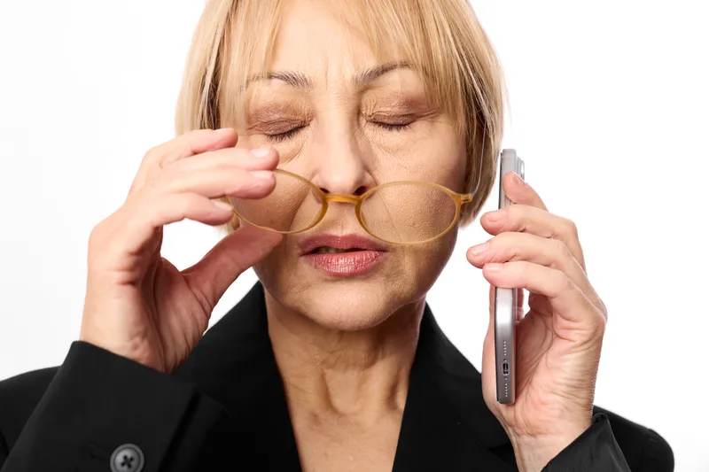 Woman with glasses holding phone and frame, eyes closed, face strained from eye strain, tired stress, communication concept of fatigue, isolated white studio