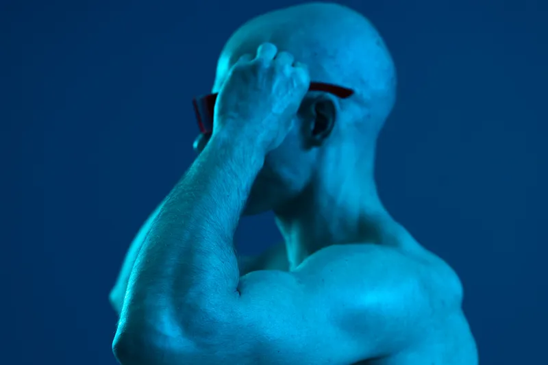 Strong man adjusting sunglasses, showcasing an athletic physique against a blue background. This striking image emphasizes confidence and style in a modern setting.