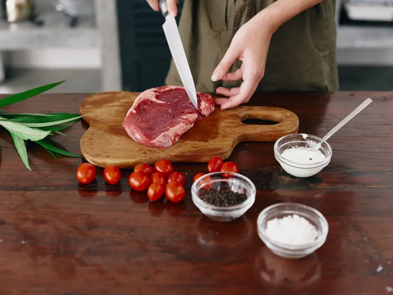 Женщина с ножом в руке нарезает мясо стейка для жарки на кухне