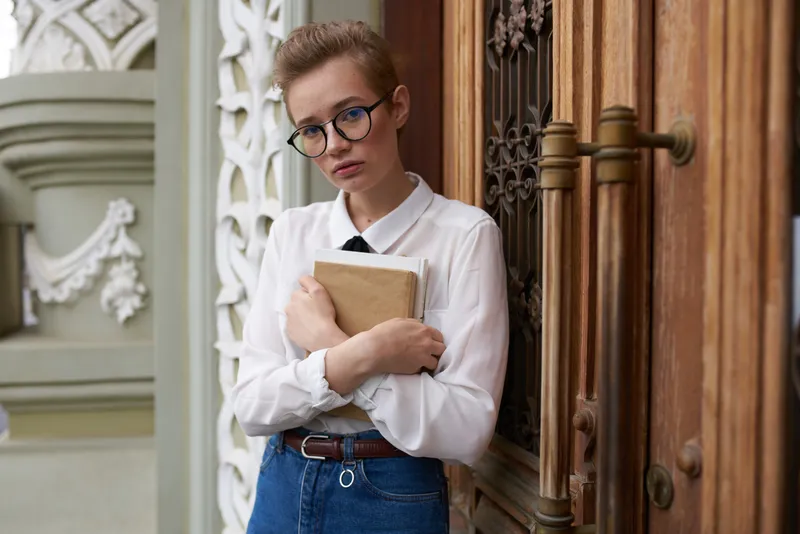Симпатичная женщина-модель в джинсах с книгой в руке стоит возле здания на улице