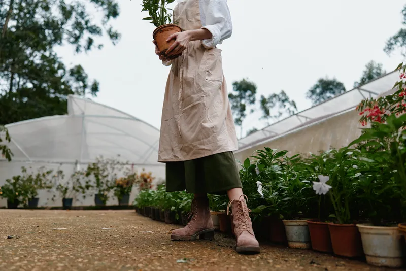 Caring gardener holding a potted plant, wearing casual work attire in a lush greenhouse environment promoting sustainability and growth
