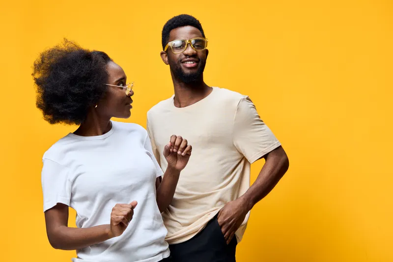 Happy young Black couple in stylish casual clothes dancing against a vibrant yellow background, showcasing joy and connection