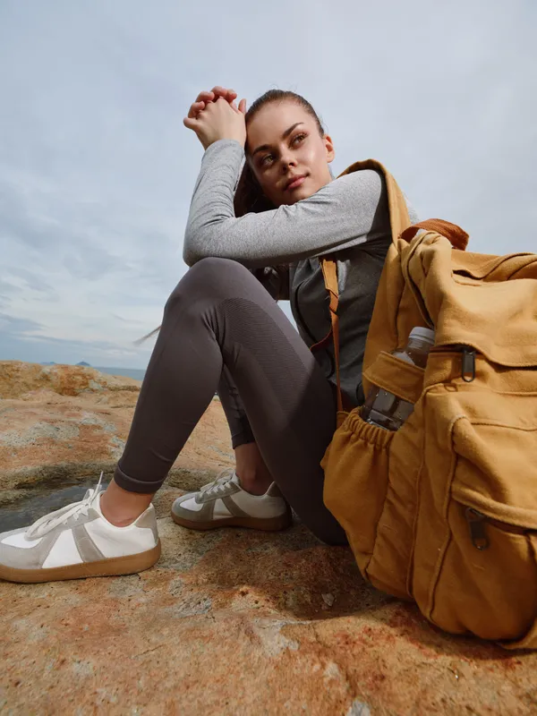 Young woman in active wear with a yellow backpack, sitting on a rocky surface, embodying adventure and outdoor exploration, perfect for travel related content