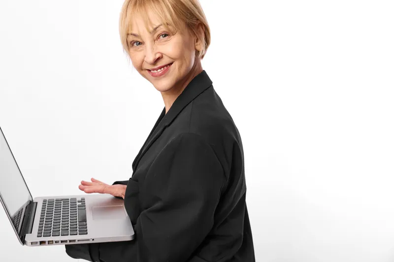 Woman with laptop in office, senior business technology communication portrait, confident older woman smiles while holding laptop on white studio background