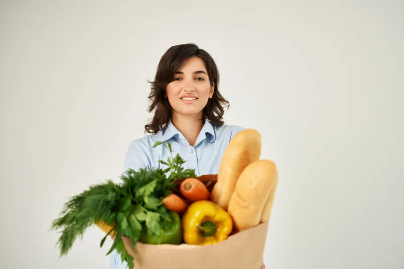 Женщина в синей рубашке упаковывает продукты в супермаркете, совершая покупки здоровой пищи