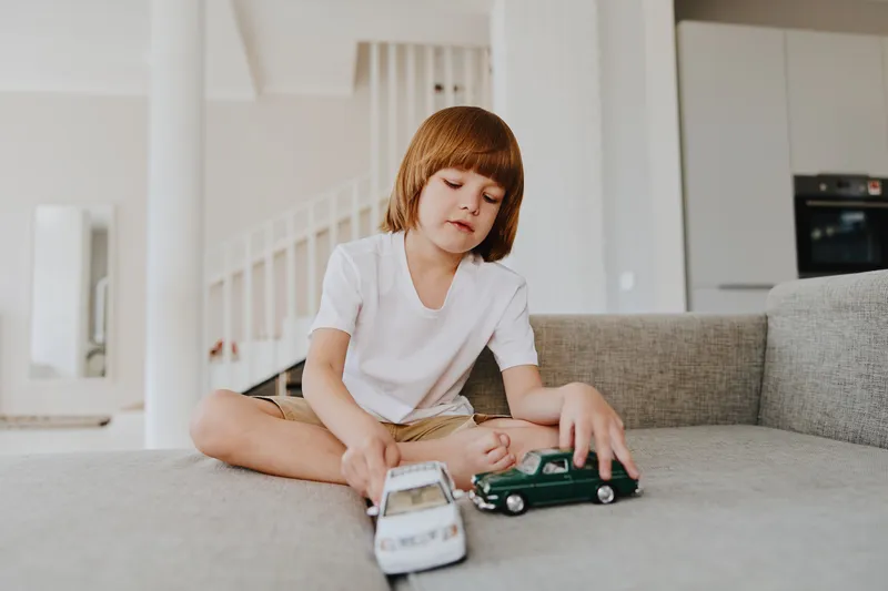 Young boy playing with toy cars in a modern living room, showcasing creativity and imagination. Ideal for family and childhood themes.