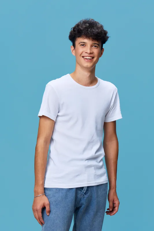 young smiling man in white t-shirt and blue jeans stands against light blue studio background, casual style, confident and friendly expression