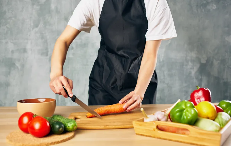Женщина в чёрном фартуке нарезает овощи на кухне, готовит свежую еду