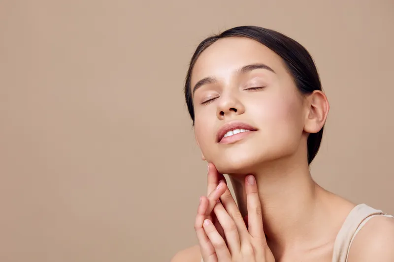 Young woman with closed eyes enjoying facial treatment, natural beauty concept, healthy skin, minimalistic beige background