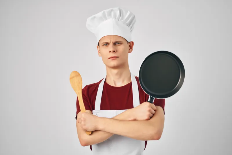 Повар-мужчина с кухонной утварью в профессиональном ресторане на светлом фоне