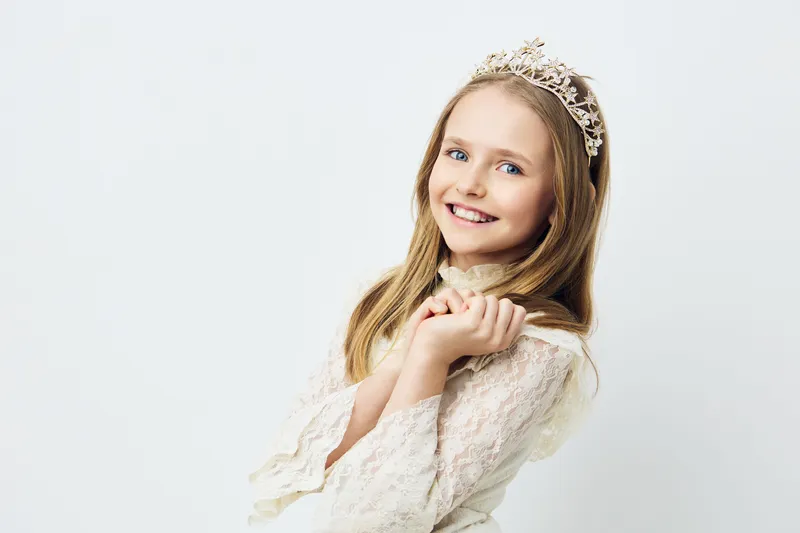 Cheerful girl in a white dress with a tiara, showcasing joy and innocence against a light background Perfect for children s fashion and fairytale themes