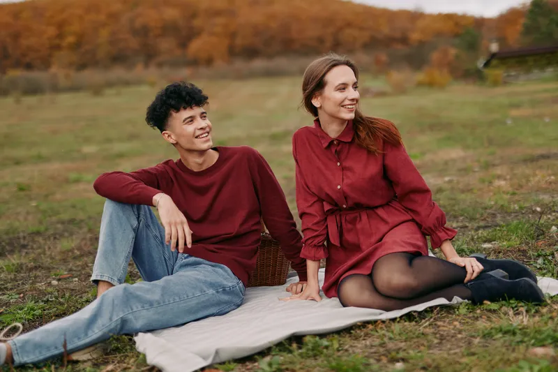 A candid outdoor portrait of a young couple on a picnic blanket, capturing genuine smiles and natural connection; this image emphasizes authenticity and credibility in everyday shared relaxed joy.