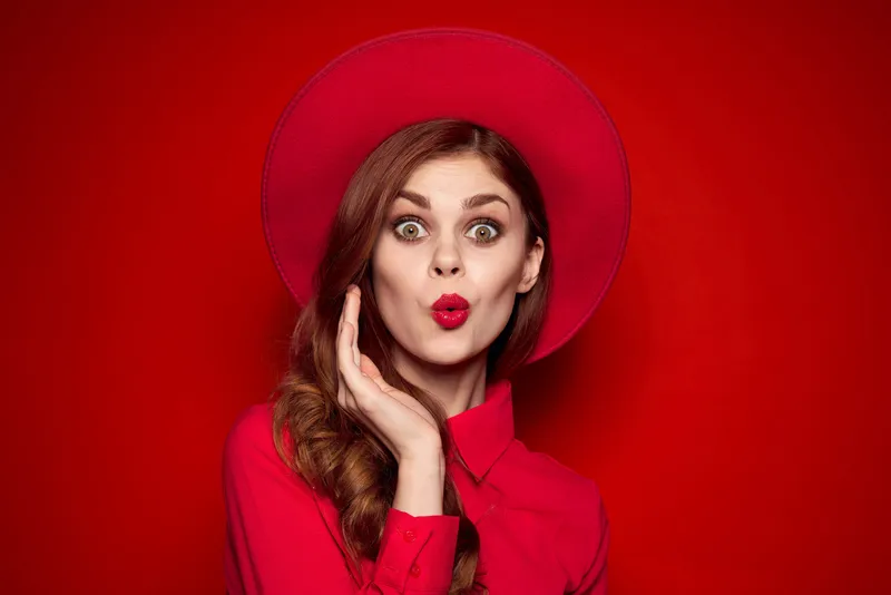 Женщина в красной рубашке с ярким макияжем и шляпой на голове