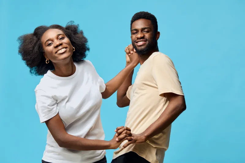 Happy young couple enjoying playful moments against a bright blue background, showcasing joy, connection, and vibrant emotions