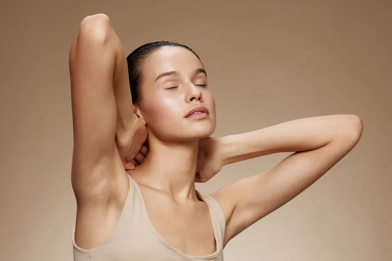 A serene portrait of a young model with smooth skin, closing her eyes and expressing tranquility against a soft beige background, showcasing natural beauty and elegance