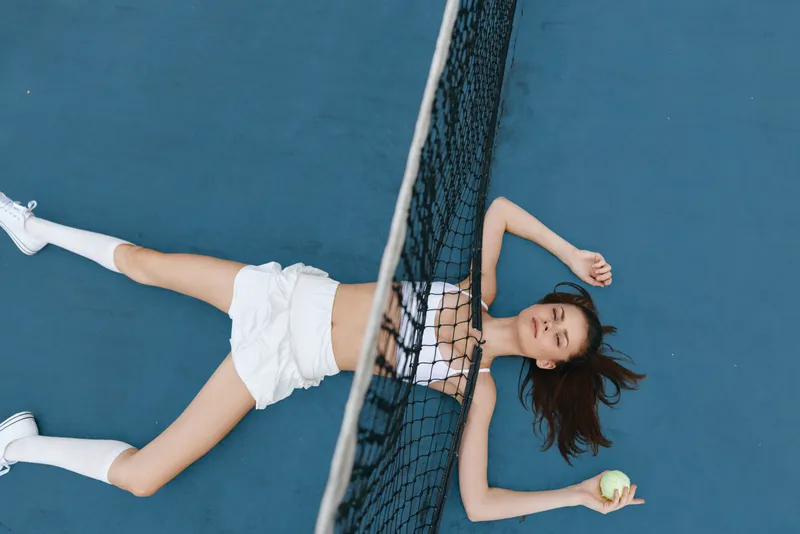 Athletic young woman relaxing on a tennis court, wearing a sporty outfit, conveying a sense of freedom and enjoyment in a vibrant blue setting