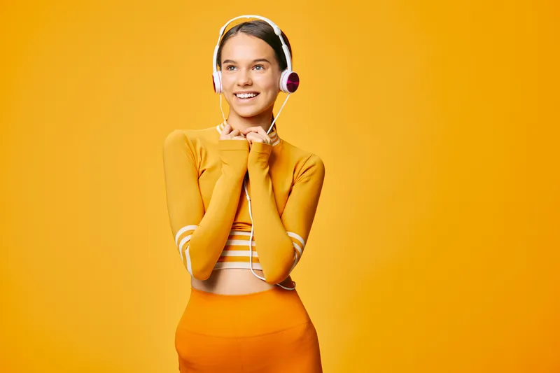 Fitness woman in bright orange outfit with striped top and headphones against a vivid orange background, posing with a confident smile ready for workout and sport lifestyle.