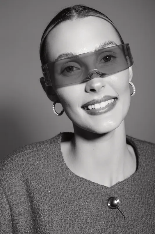 Portrait of a young white woman with pale skin wearing transparent oversized glasses and hoop earrings smiling in studio. Concept for fashion and eyewear.