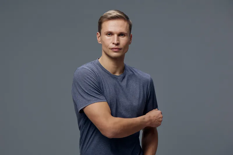 Confident young man with fair skin and short hair wearing casual blue t-shirt standing against gray background studio portrait. People lifestyle concept