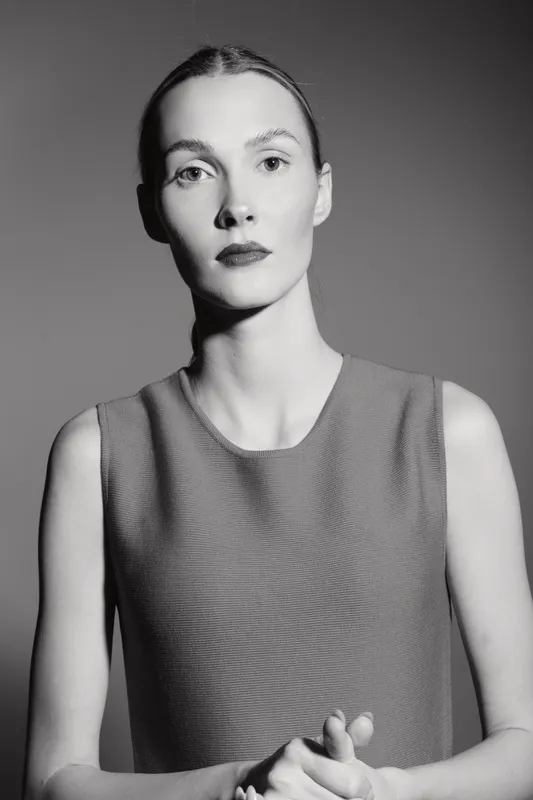 Portrait of a pale white woman with blonde hair in a textured sleeveless top, looking confidently at the camera in black and white studio lighting.
