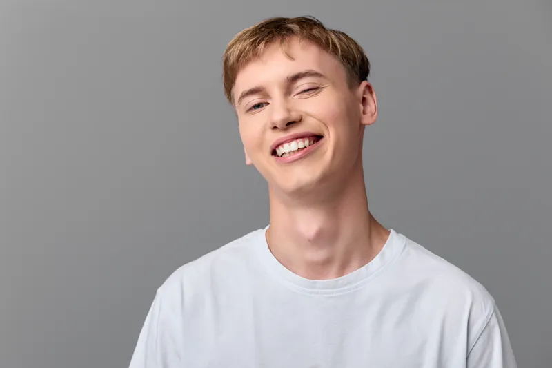 Smiling young man in a white tshirt against a gray backdrop, conveying casual confidence, friendly vibe, modern simplicity, and approachable style for lifestyle, fashion, and stock photography