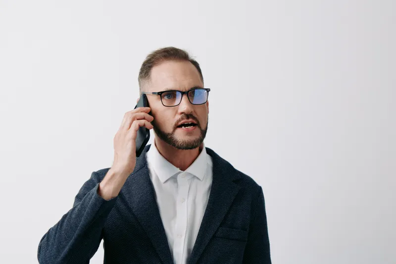 A professional businessman speaks on a mobile phone, showing confidence and focus, against an isolated white color background suitable for corporate media and leadership imagery.